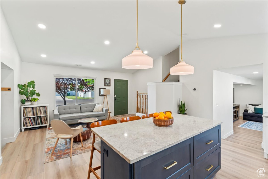 Kitchen featuring open floor plan, light wood finished floors, a kitchen bar, light stone countertops, and recessed lighting