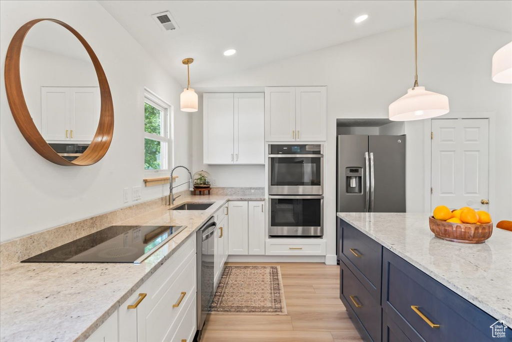 Kitchen featuring vaulted ceiling, appliances with stainless steel finishes, white cabinetry, a sink, and light stone counters