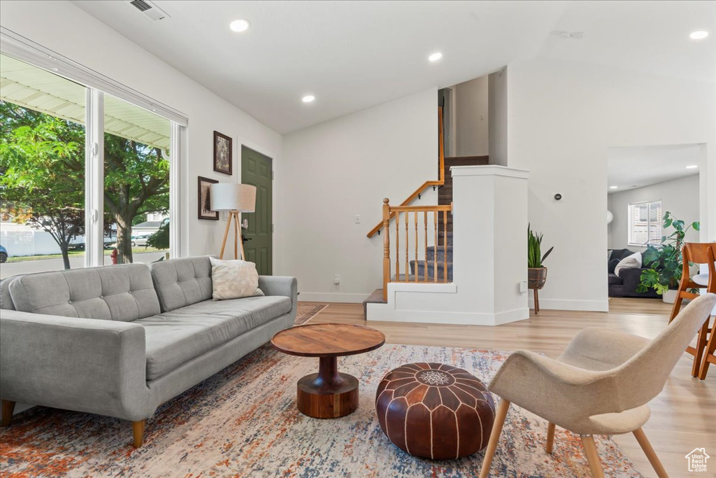 Living area featuring stairs, light wood-type flooring, recessed lighting, baseboards, and vaulted ceiling