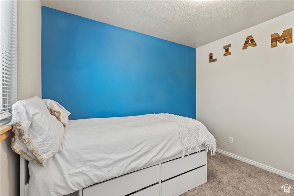 Bedroom featuring light carpet, baseboards, and a textured ceiling