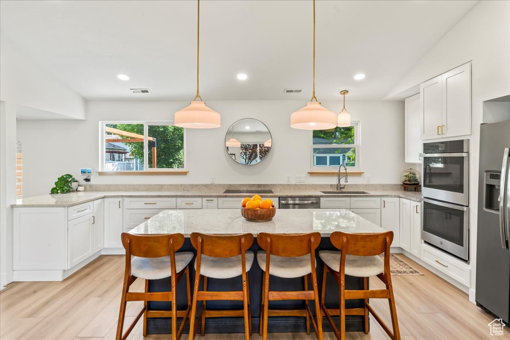 Kitchen with a sink, appliances with stainless steel finishes, white cabinets, light wood finished floors, and recessed lighting
