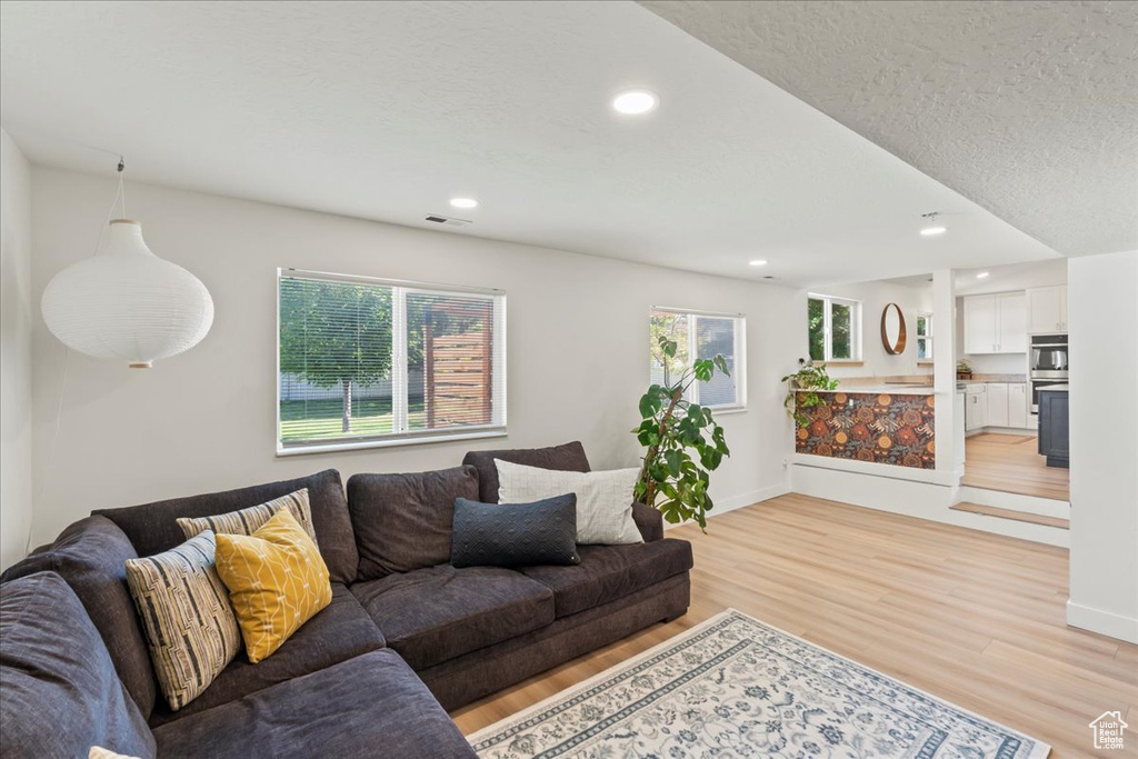Living area featuring light wood finished floors, baseboards, recessed lighting, and a textured ceiling