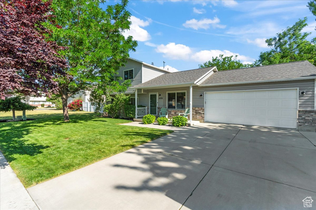 View of front of property featuring an attached garage, driveway, a front lawn, and roof with shingles