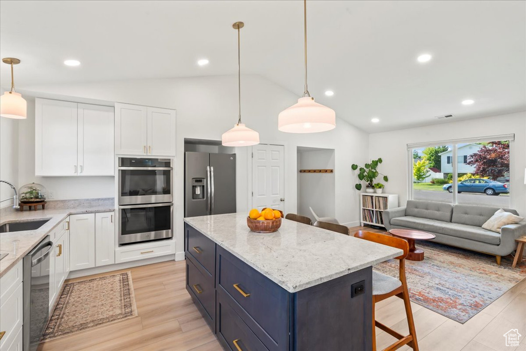 Kitchen featuring stainless steel appliances, vaulted ceiling, white cabinetry, a sink, and light wood-style flooring