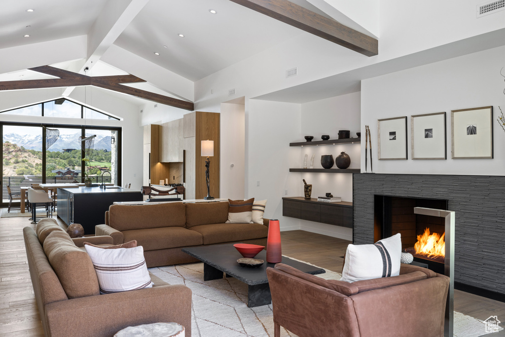 Living room featuring beam ceiling, light wood finished floors, a fireplace, and high vaulted ceiling