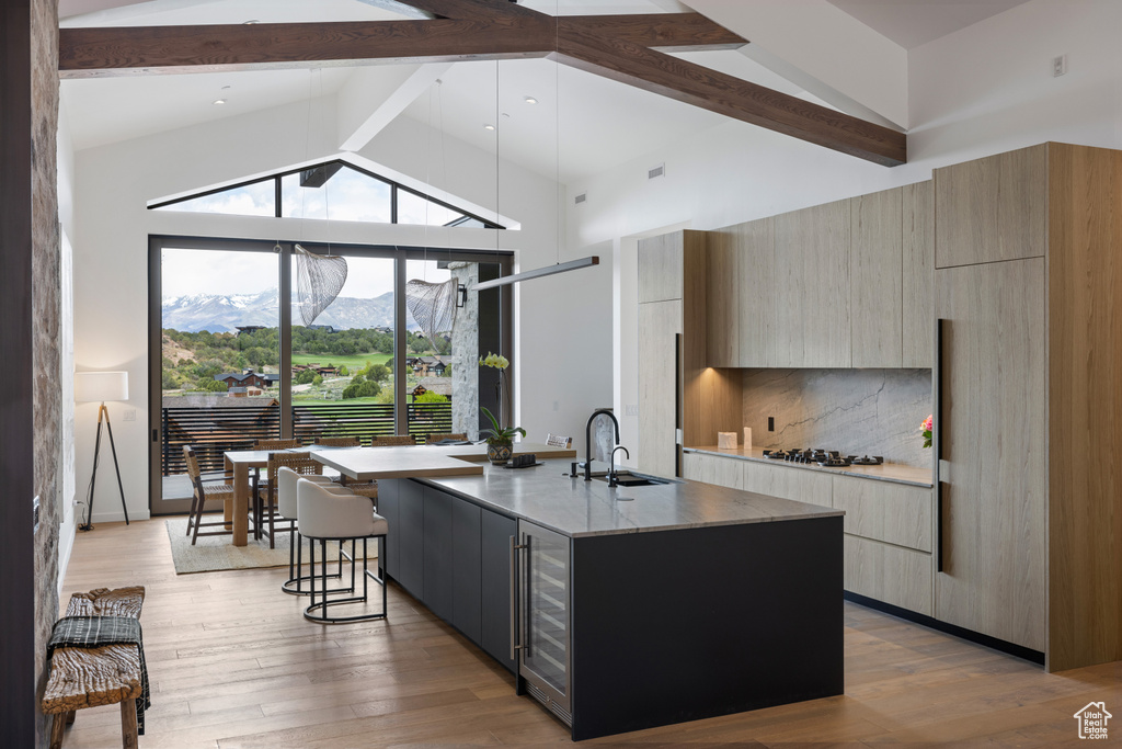Kitchen with modern cabinets, a sink, beam ceiling, beverage cooler, and a large island with sink