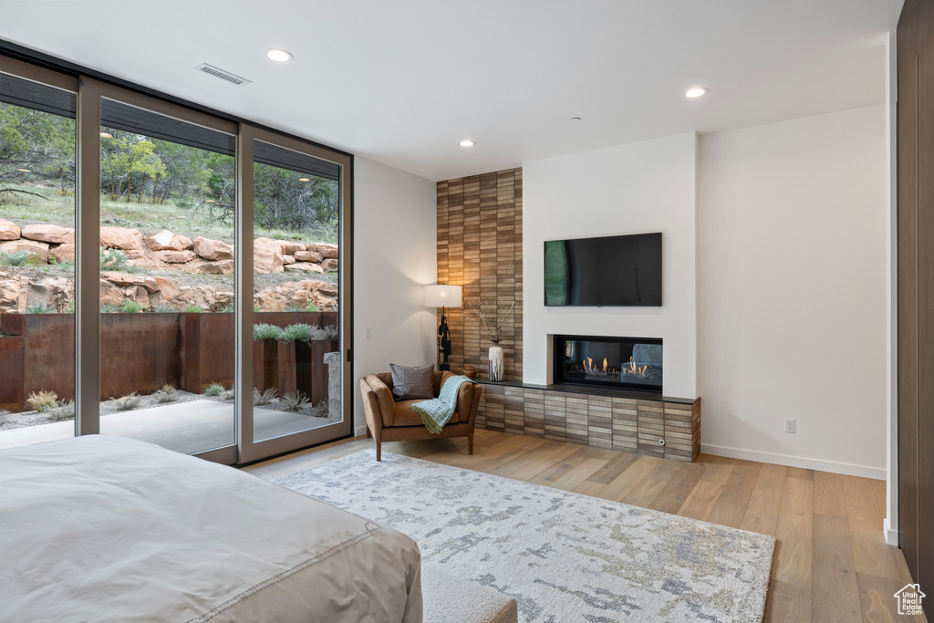 Bedroom with wood finished floors, baseboards, access to exterior, recessed lighting, and a glass covered fireplace