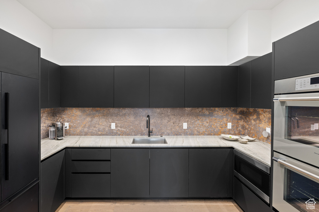 Kitchen featuring a sink, built in appliances, dark cabinetry, and backsplash