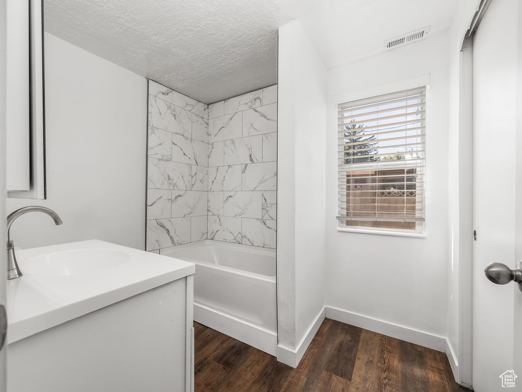 Full bathroom featuring baseboards, wood finished floors, vanity, a textured ceiling, and bathtub / shower combination
