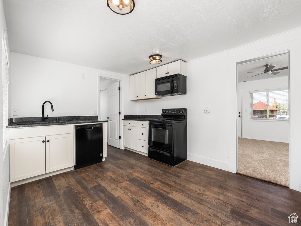 Kitchen with black appliances, a sink, white cabinets, dark wood-style floors, and dark stone countertops