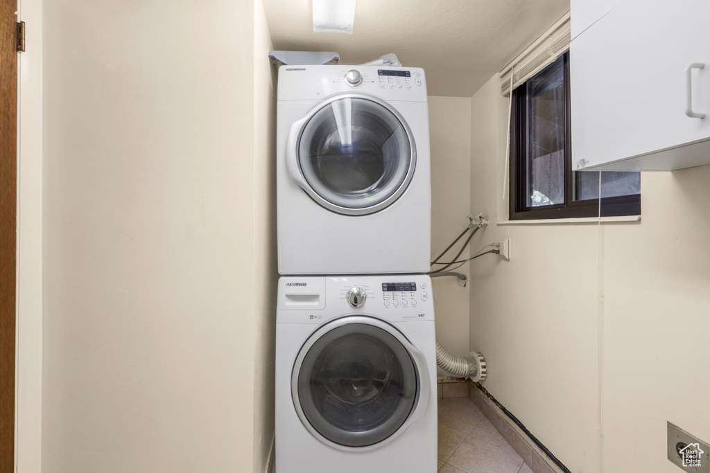 Washroom with cabinet space, stacked washer / dryer, tile patterned flooring, and baseboards