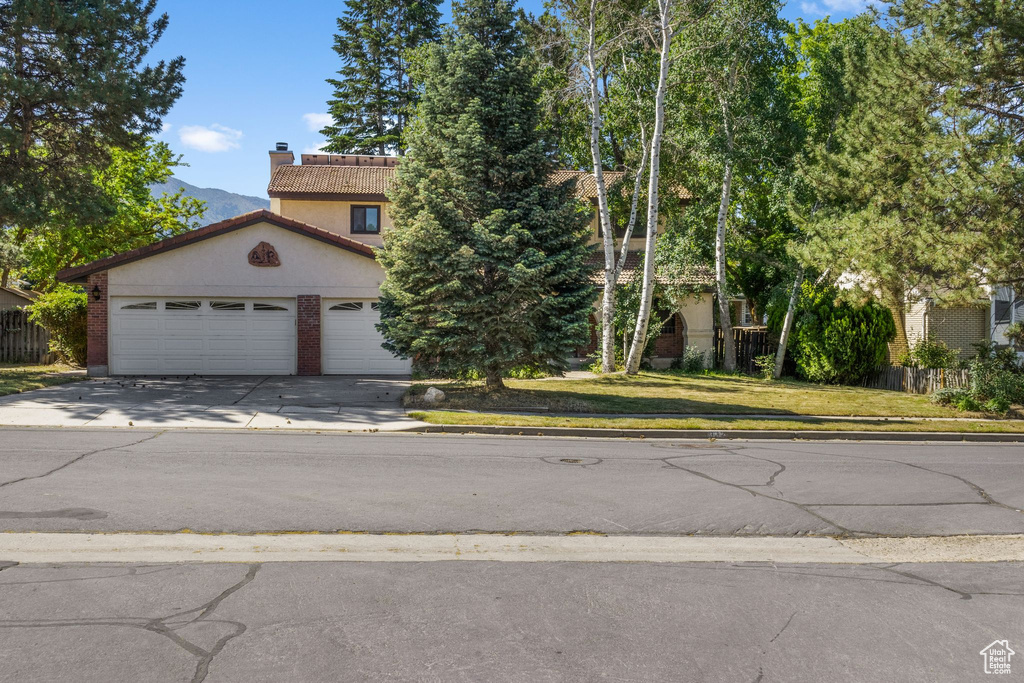 View of front of property featuring driveway, a chimney, an attached garage, and a tiled roof
