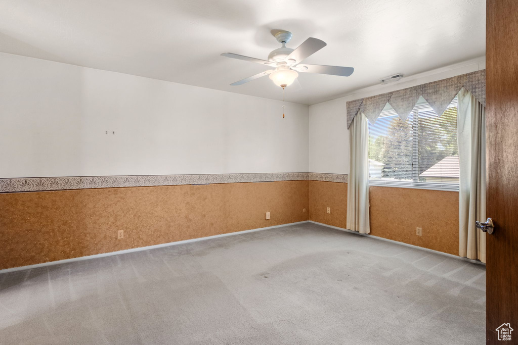 Empty room featuring carpet, ceiling fan, and a wainscoted wall