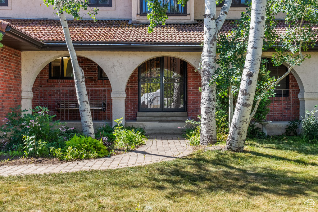 View of exterior entry with a lawn, a porch, brick siding, stucco siding, and a tile roof