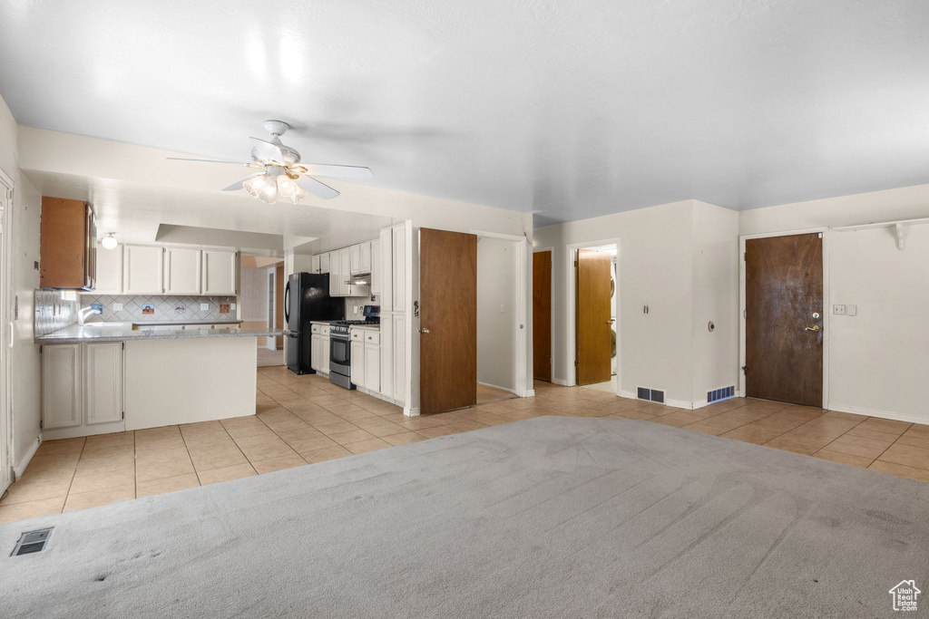 Kitchen with stainless steel gas range, light tile patterned flooring, freestanding refrigerator, ceiling fan, and decorative backsplash