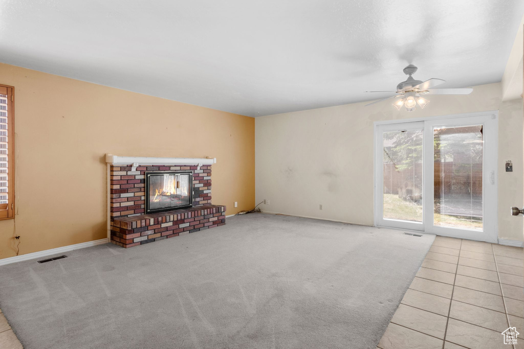 Unfurnished living room with ceiling fan, a brick fireplace, baseboards, carpet flooring, and tile patterned floors