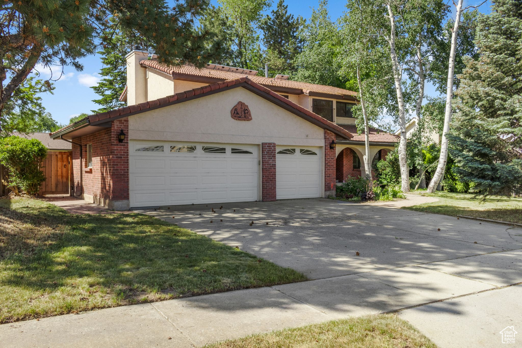 Mediterranean / spanish home featuring an attached garage, concrete driveway, a chimney, and brick siding