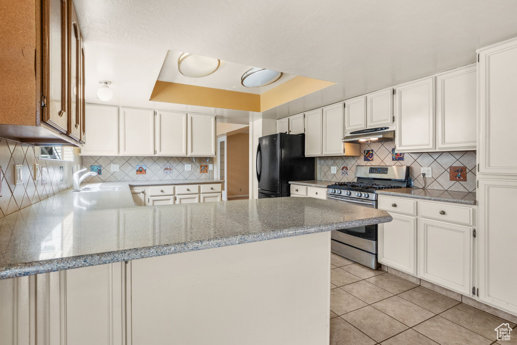 Kitchen featuring stainless steel gas range, freestanding refrigerator, under cabinet range hood, a peninsula, and light tile patterned floors