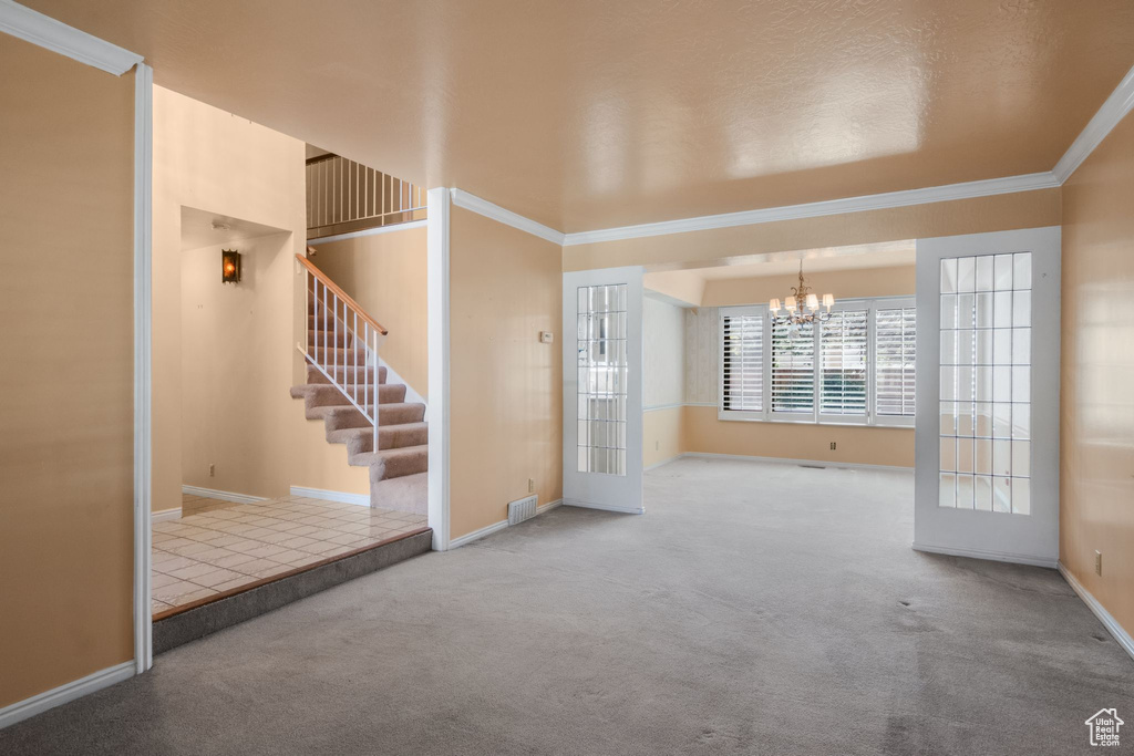 Unfurnished living room with a chandelier, crown molding, carpet floors, stairs, and baseboards
