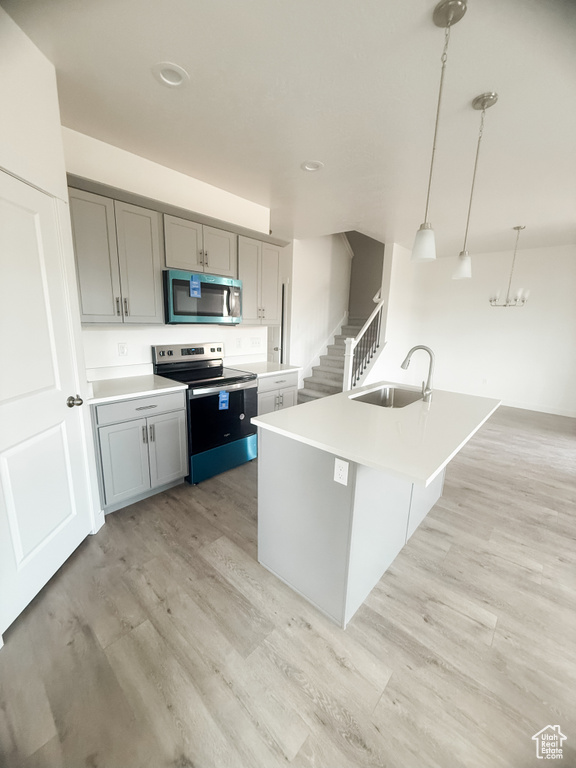 Kitchen with appliances with stainless steel finishes, a sink, light wood-style floors, light countertops, and gray cabinetry