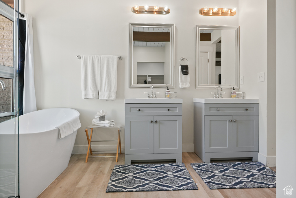Bathroom featuring wood finished floors, two vanities, baseboards, and a freestanding tub