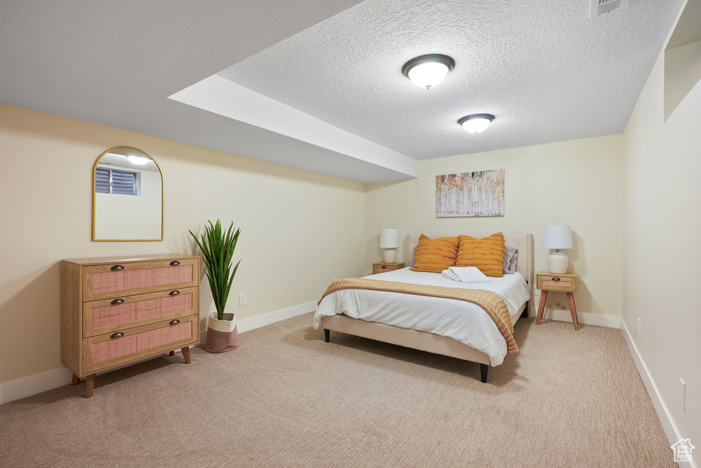 Bedroom with light carpet, a textured ceiling, and baseboards