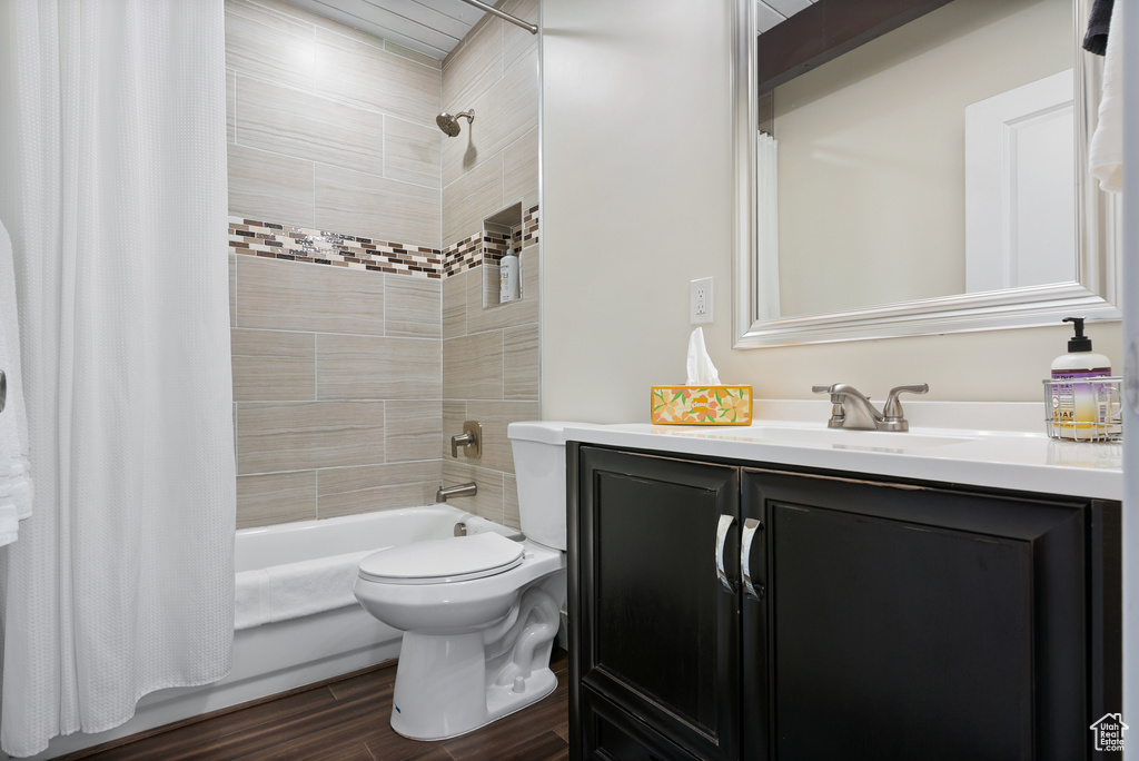 Bathroom with shower / bathtub combination with curtain, vanity, wood finished floors, and toilet