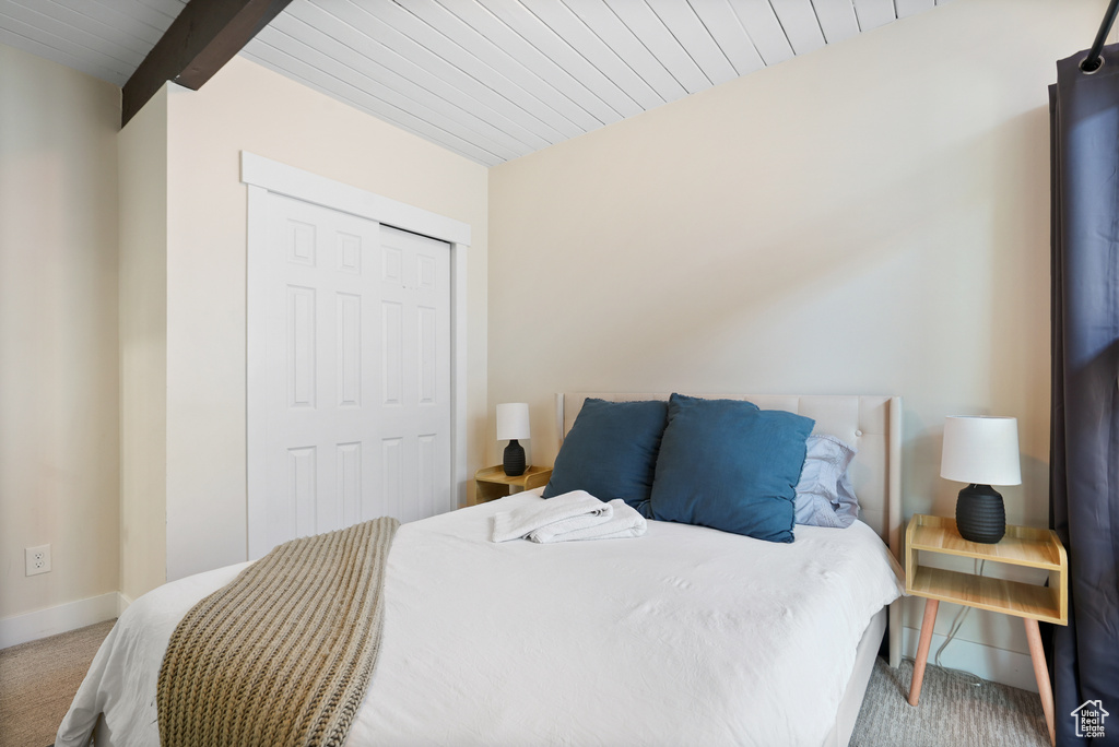 Bedroom with carpet flooring, a closet, baseboards, and wood ceiling with exposed beams