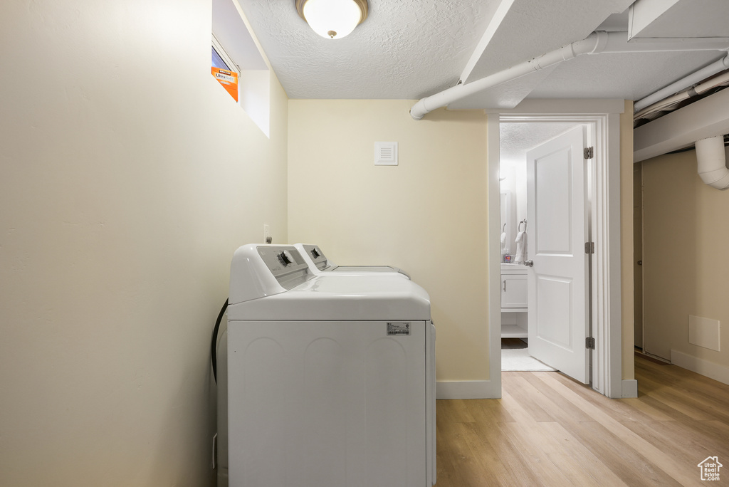 Washroom featuring washer and dryer, light wood-style floors, a textured ceiling, and baseboards