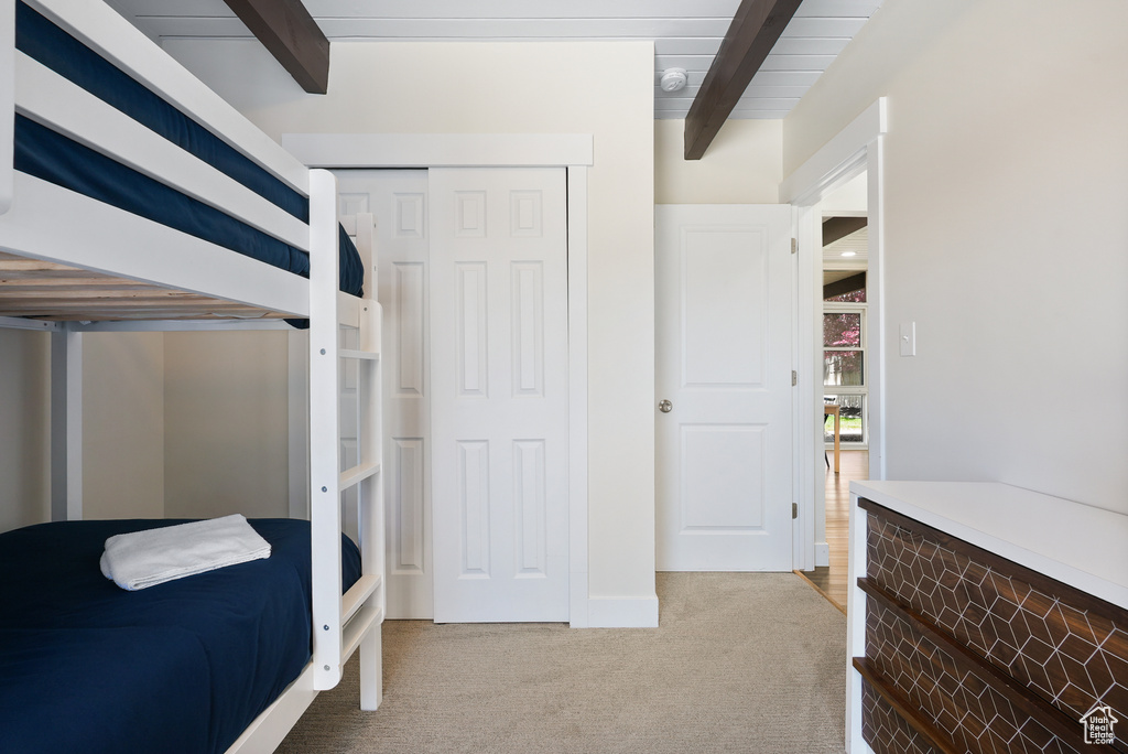 Bedroom featuring light carpet, a closet, and beamed ceiling