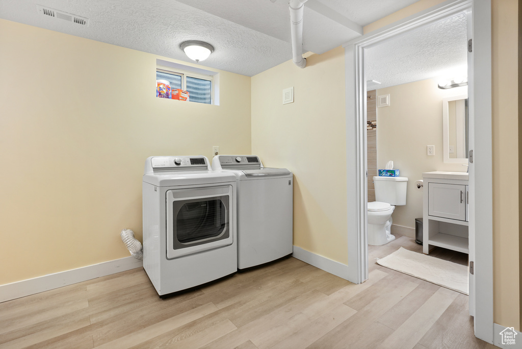Washroom featuring washer and clothes dryer, light wood finished floors, a textured ceiling, and baseboards
