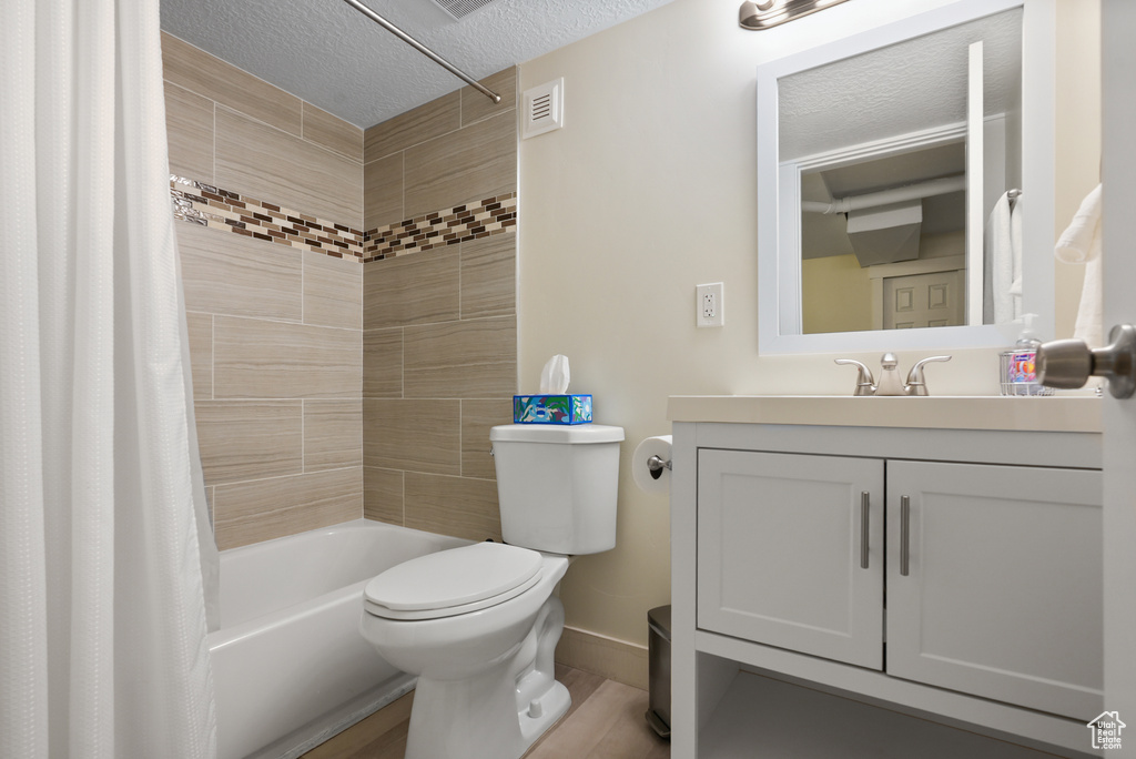 Full bath featuring toilet, a textured ceiling, shower / tub combo with curtain, vanity, and baseboards