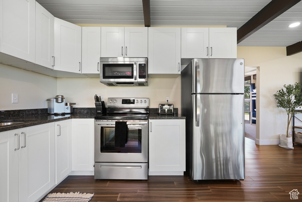 Kitchen featuring stainless steel appliances, white cabinets, beamed ceiling, and dark wood finished floors
