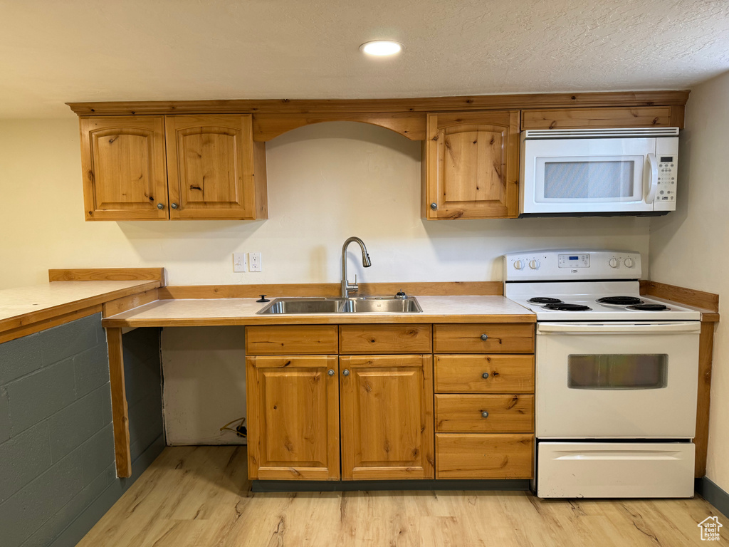 Kitchen with white appliances, a sink, light wood-type flooring, light countertops, and brown cabinetry