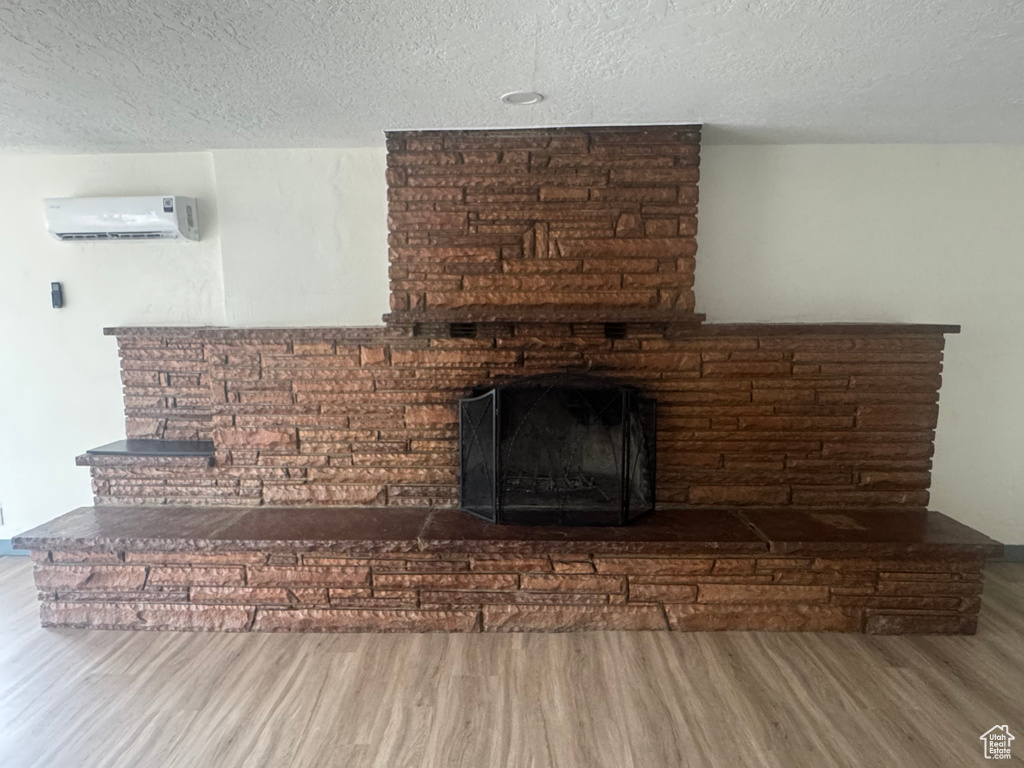 Detailed view of a wall mounted AC, wood finished floors, a textured ceiling, and a fireplace