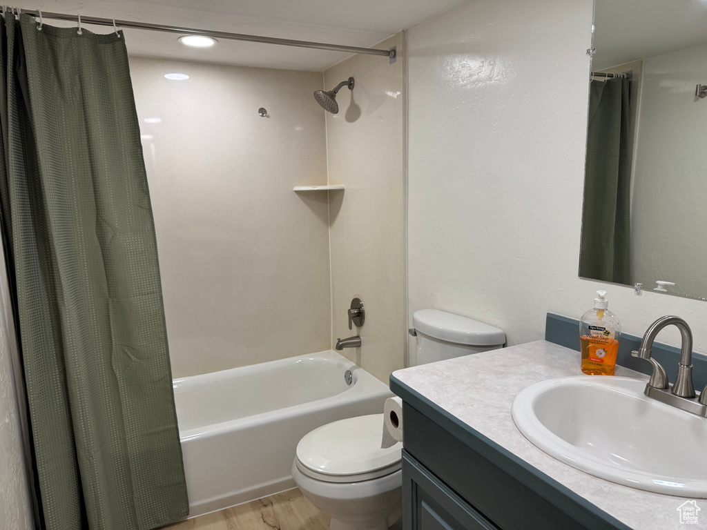Bathroom featuring toilet, shower / tub combo, vanity, and wood finished floors