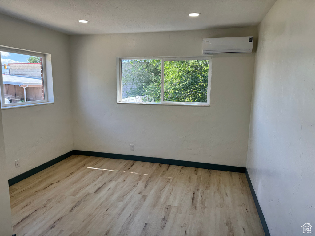 Empty room featuring a wall unit AC, wood finished floors, baseboards, and recessed lighting