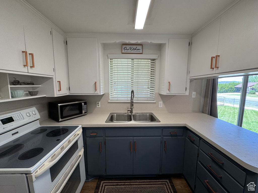 Kitchen featuring white range with electric stovetop, a sink, stainless steel microwave, light countertops, and white cabinetry
