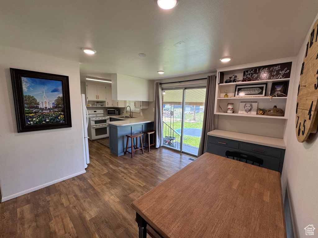 Kitchen featuring range with two ovens, a sink, light countertops, dark wood-type flooring, and a kitchen bar