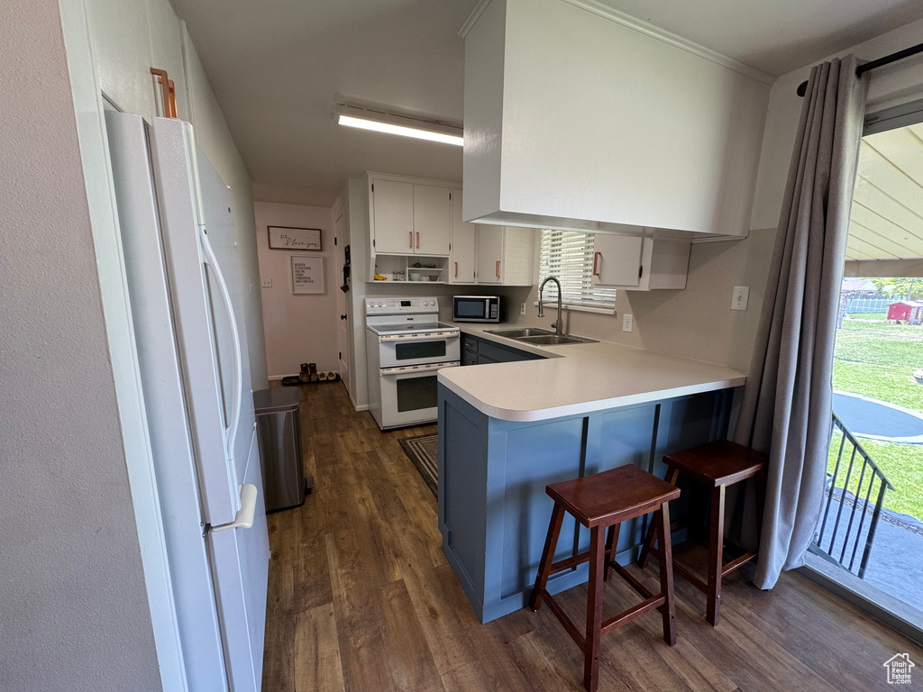 Kitchen featuring white appliances, a sink, dark wood-type flooring, a peninsula, and white cabinetry