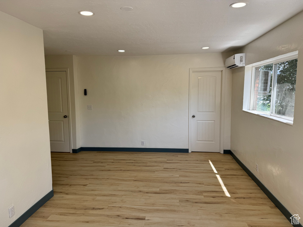 Empty room featuring a wall mounted AC, baseboards, recessed lighting, and light wood finished floors