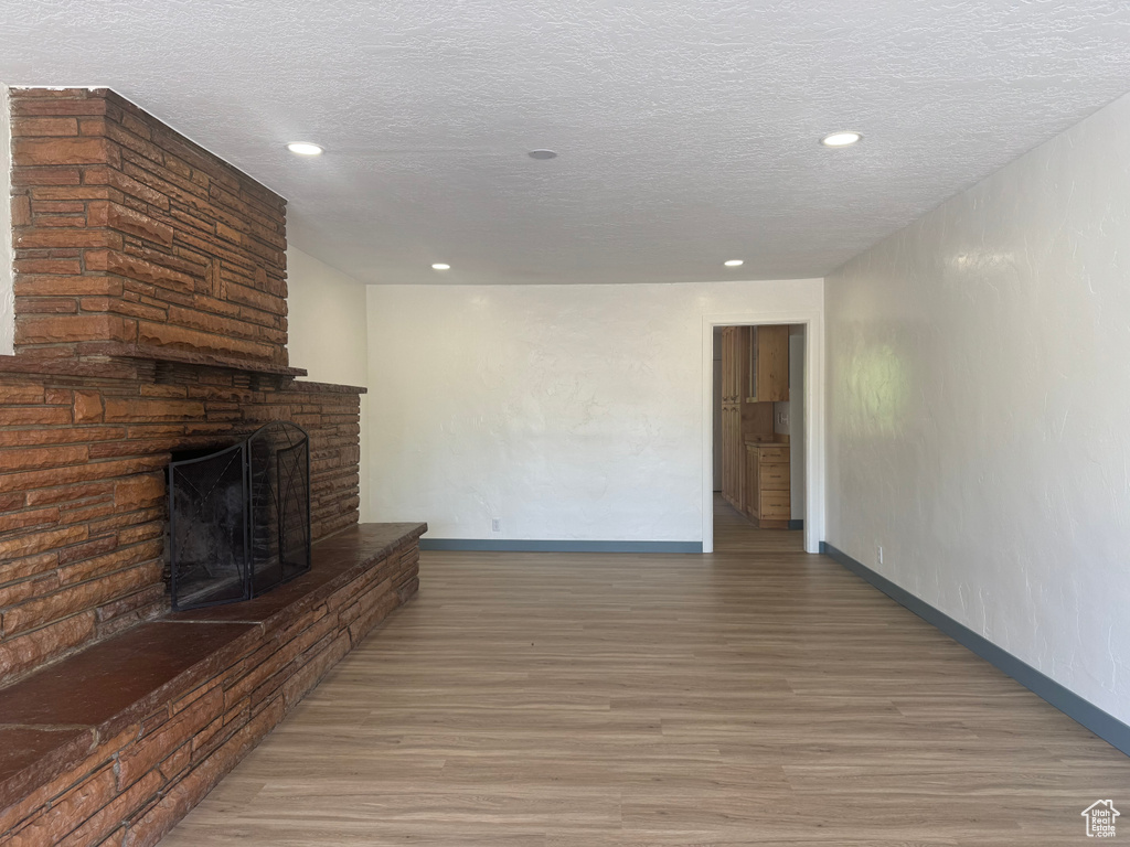 Unfurnished living room featuring wood finished floors, a fireplace, recessed lighting, baseboards, and a textured ceiling