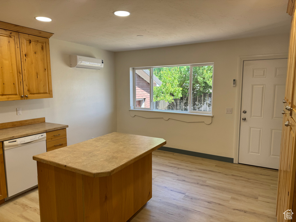 Kitchen with dishwasher, a wall mounted air conditioner, light countertops, light wood finished floors, and a kitchen island