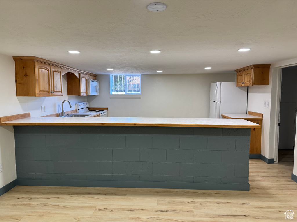 Kitchen with white appliances, a peninsula, light wood finished floors, a sink, and recessed lighting