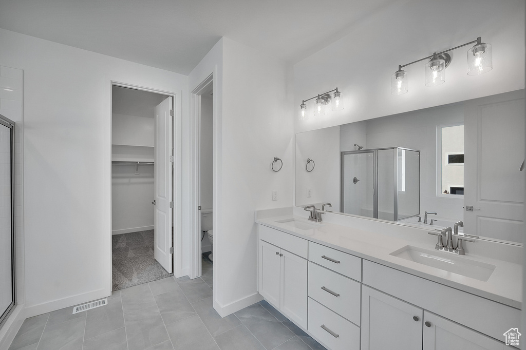 Full bath with a shower stall, toilet, double vanity, a spacious closet, and tile patterned flooring