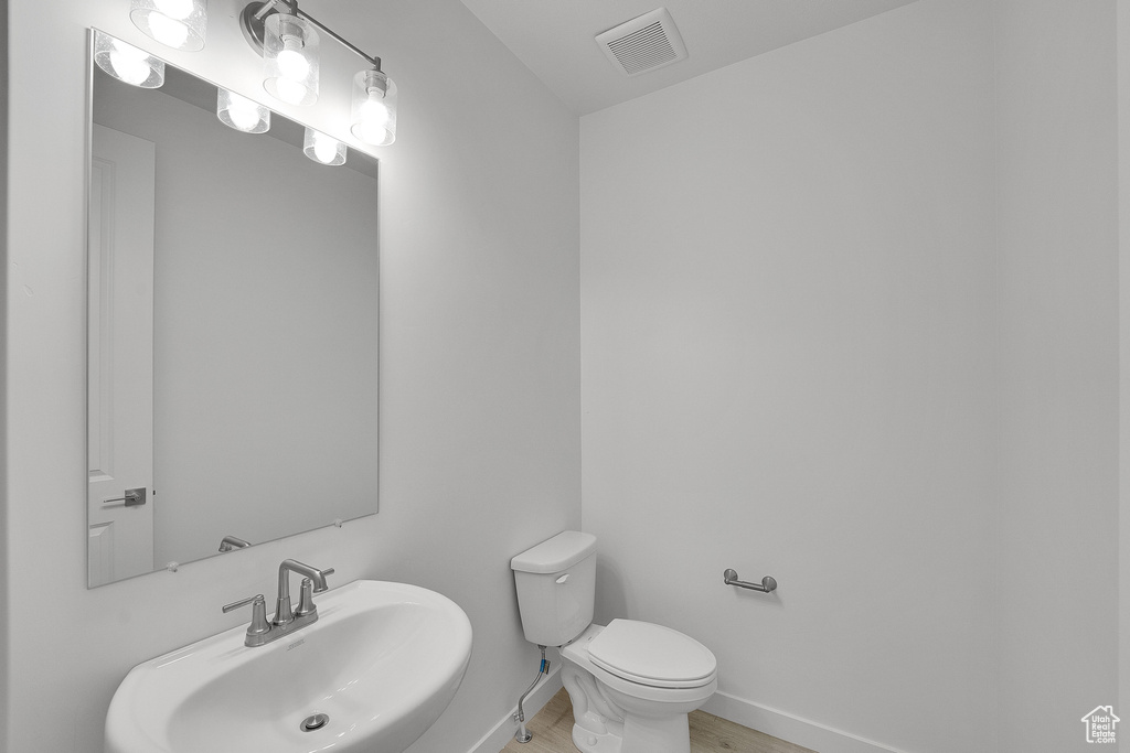 Half bath featuring a sink, toilet, baseboards, and wood finished floors