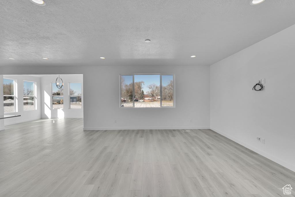 Unfurnished living room featuring a textured ceiling, light wood-type flooring, recessed lighting, and baseboards