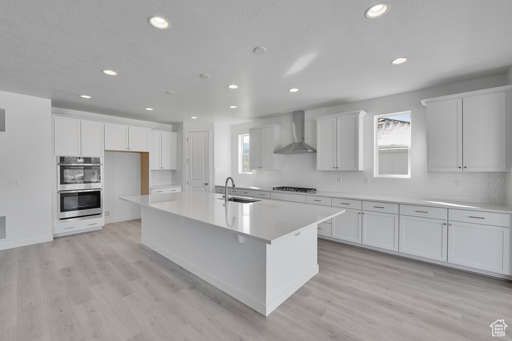 Kitchen with a sink, wall chimney exhaust hood, double oven, backsplash, and recessed lighting