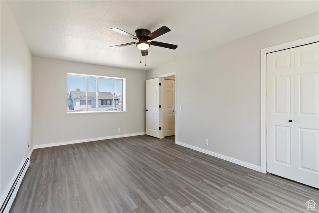 Unfurnished bedroom featuring a baseboard heating unit, wood finished floors, baseboards, ceiling fan, and a closet