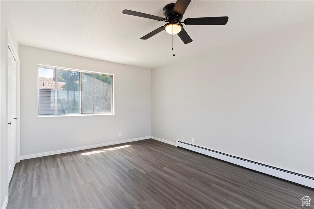 Spare room with baseboard heating, dark wood-type flooring, baseboards, and ceiling fan